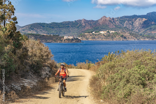 nice woman riding her electric mountain bike on the coastline above the mediterranean sea on the Island of Elba in the tuscan Archipelago  Tuscany  Italy