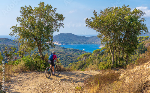 nice woman riding her electric mountain bike on the coastline above the mediterranean sea on the Island of Elba in the tuscan Archipelago, Tuscany, Italy