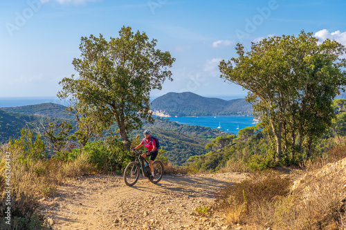 Fototapeta Naklejka Na Ścianę i Meble -  nice woman riding her electric mountain bike on the coastline above the mediterranean sea on the Island of Elba in the tuscan Archipelago, Tuscany, Italy