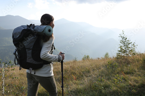 Tourist with backpack and trekking poles hiking through mountains, space for text