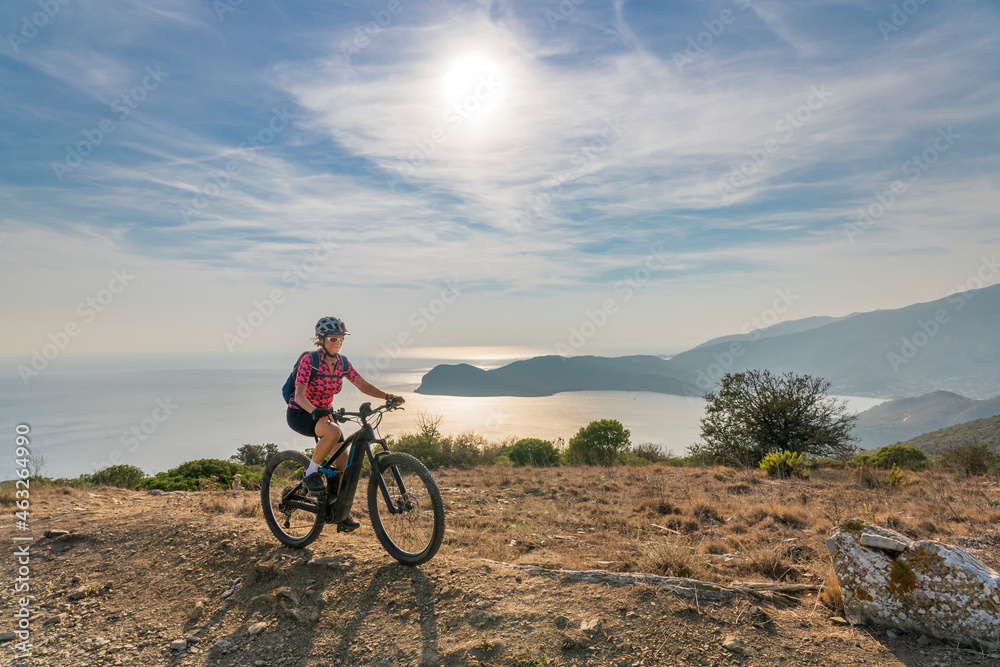 nice woman riding her electric mountain bike at sunset at the coastline of mediterranean sea on the Island of Elba in the tuscan Archipelago Tuscany, Italy