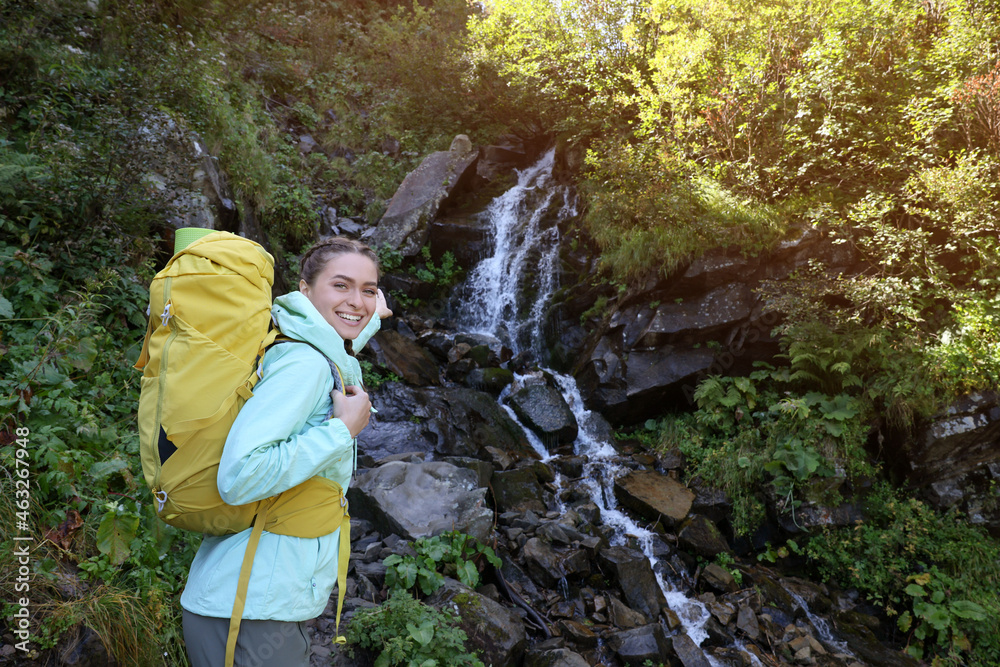 Tourist with backpack near waterfall in mountains. Space for text