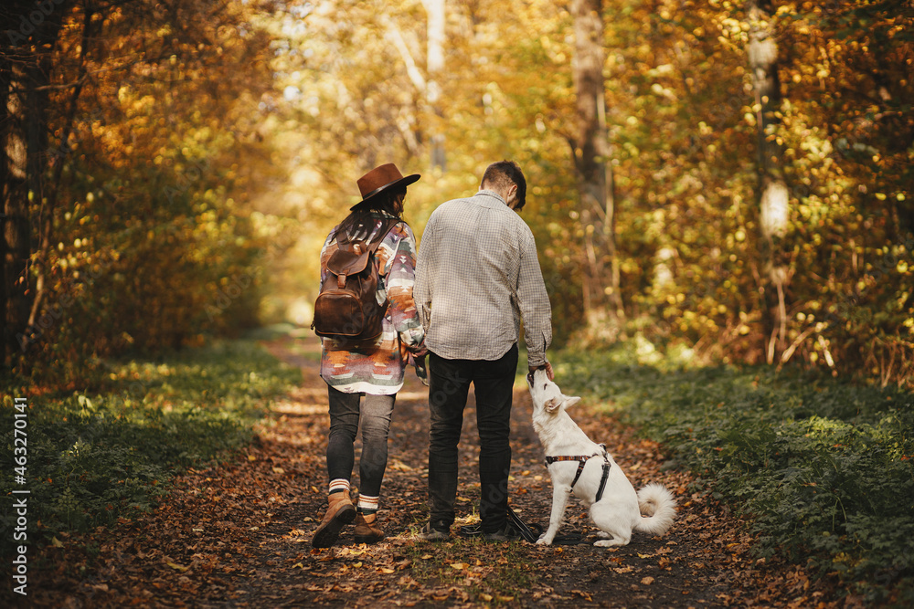 Stylish couple hiking with cute dog in sunny autumn woods. Young hipster family travelling with swiss shepherd white dog. Traveling with pet, loyal companion. Travel and Wanderlust Stylish couple hiking with cute dog in sunny autumn woods. Young hipster family travelling with swiss shepherd white dog. Traveling with pet, loyal companion. Travel and Wanderlust
