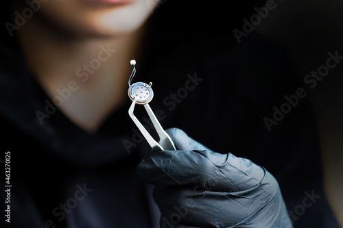 Spy games. Small microphone of the overhearing device, spy holding a microphone with tweezers, black gloves. Micro listening device