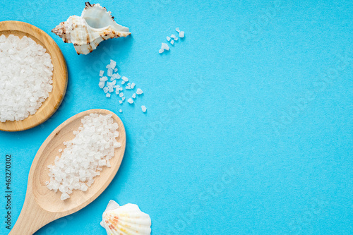 Sea salt, wooden spoon, shells on blue surface. Flat lay with crystals of salt, top view, space for text