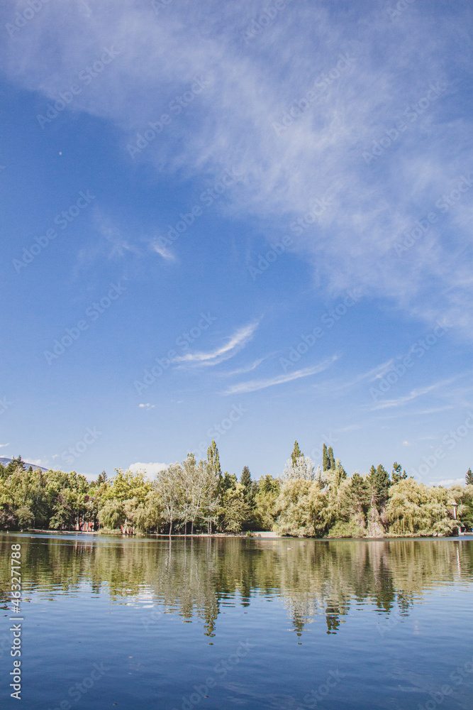 Fototapeta premium Reflejo Lago con barcas arboles y cielo azul con nubes colores