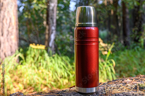 Steel red camping thermos with hot tea in the forest