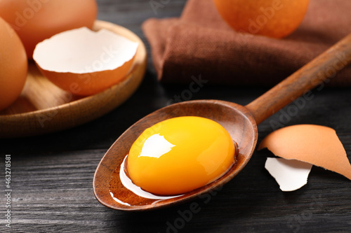 Tableau sur toile Spoon with raw egg yolk on black wooden table, closeup