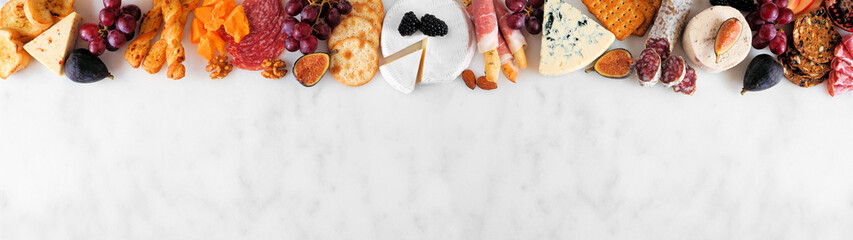Variety of cheese and meat appetizers. Above view top border on a white marble banner background with copy space.