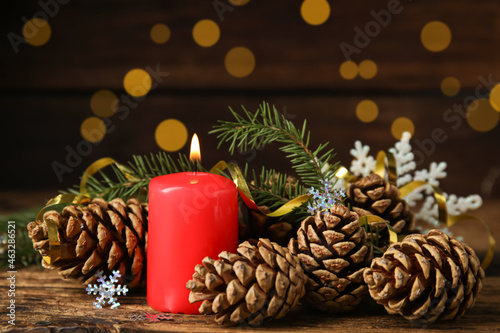 Burning candle, pine cones and fir tree branches on wooden table against blurred festive lights. Christmas eve