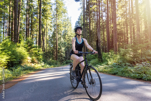 Adventurous White Caucasian Woman on a bicycle riding on a path in Green Canadian Rain Forest. Seymour Valley Trailway in North Vancouver, British Columbia, Canada.