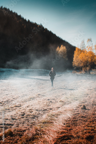 A active outdoor female girl exploring and walking on a white frozen meadow in the mountain. Early morning exploring the sunrise mountains with calm and peaceful vibes with orange autumn sunrise color