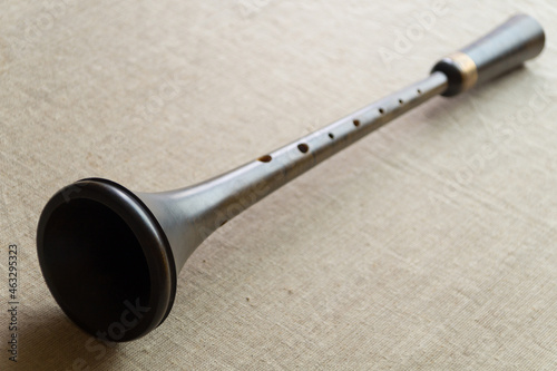 Shawm (schalmei, schalmeien) , a brown medieval wooden folk wind musical instrument with a metal decor, lies on a gray canvas photo