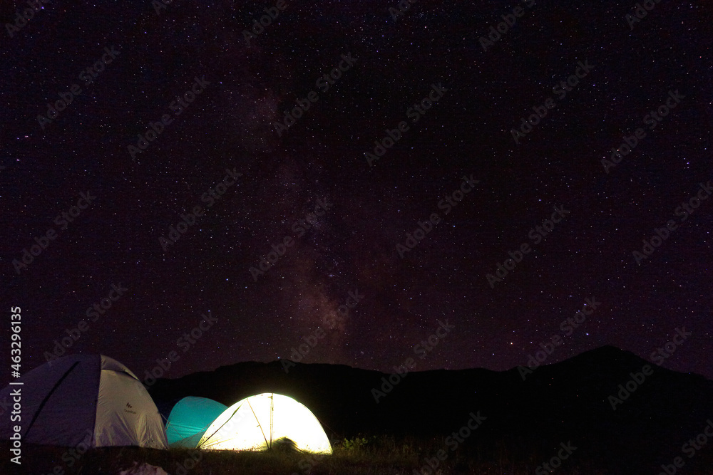 Milky Way galaxy over mountains and tourist camp in the starry night sky. Caucasian State Natural Biosphere Reserve named after Kh.G. Shaposhnikov. Tract Instructor's gap.