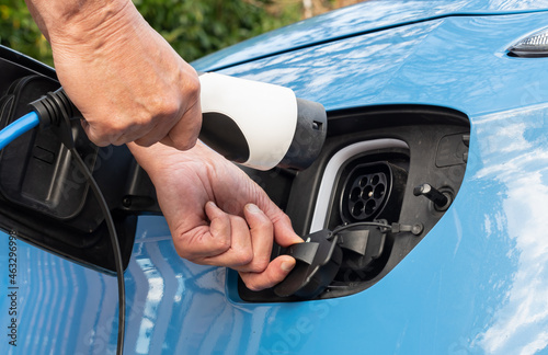 Close up view of front end of a blue electric E car showing mans hands connecting a type 2 charge plug and socket and granny cable