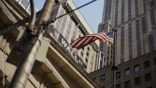 Wall Street sign with American flags in the background, shot in the heart of the business world in Manhattan. Business, finance, worldwide stock trade and economics concept.