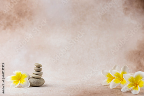 Pyramids of gray and white zen pebble meditation stones on beige background with plumeria tropical flower. Concept of harmony, balance and meditation, spa, massage, relax