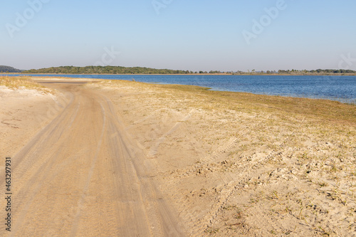 Dirty road with lake, sand and vegetation photo