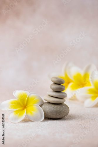 Pyramids of gray and white zen pebble meditation stones on beige background with plumeria tropical flower. Concept of harmony, balance and meditation, spa, massage, relax