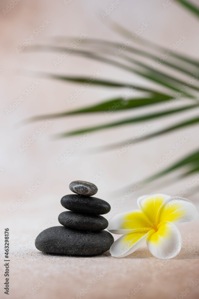 Fototapeta premium Pyramids of gray and white zen pebble meditation stones on beige background with plumeria tropical flower. Concept of harmony, balance and meditation, spa, massage, relax