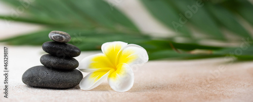 Pyramids of gray and white zen pebble meditation stones on beige background with plumeria tropical flower. Concept of harmony, balance and meditation, spa, massage, relax. Banner format