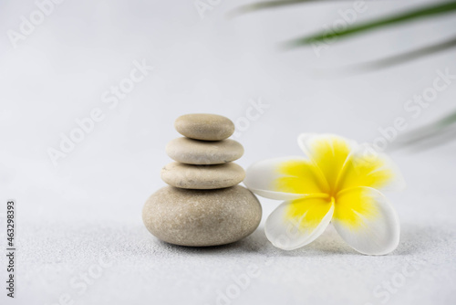 Pyramids of gray and white zen pebble meditation stones on white background with plumeria tropical flower. Concept of harmony, balance and meditation, spa, massage, relax