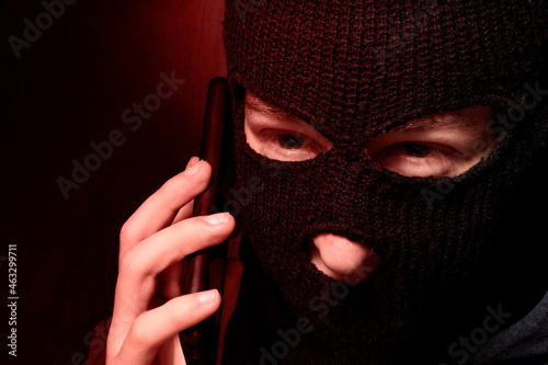 A man in a balaclava is talking on a mobile phone. The concept of Internet fraud, hacking of payment systems, hacking of electronic wallets © Наталья Устинова