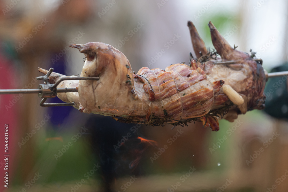 rabbit covered with strips of side bacon on a wooden fire