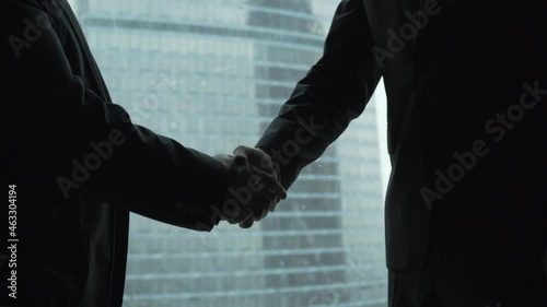 Close-up of three silhouettes of businessmen shaking hands in Moscow city office near the window