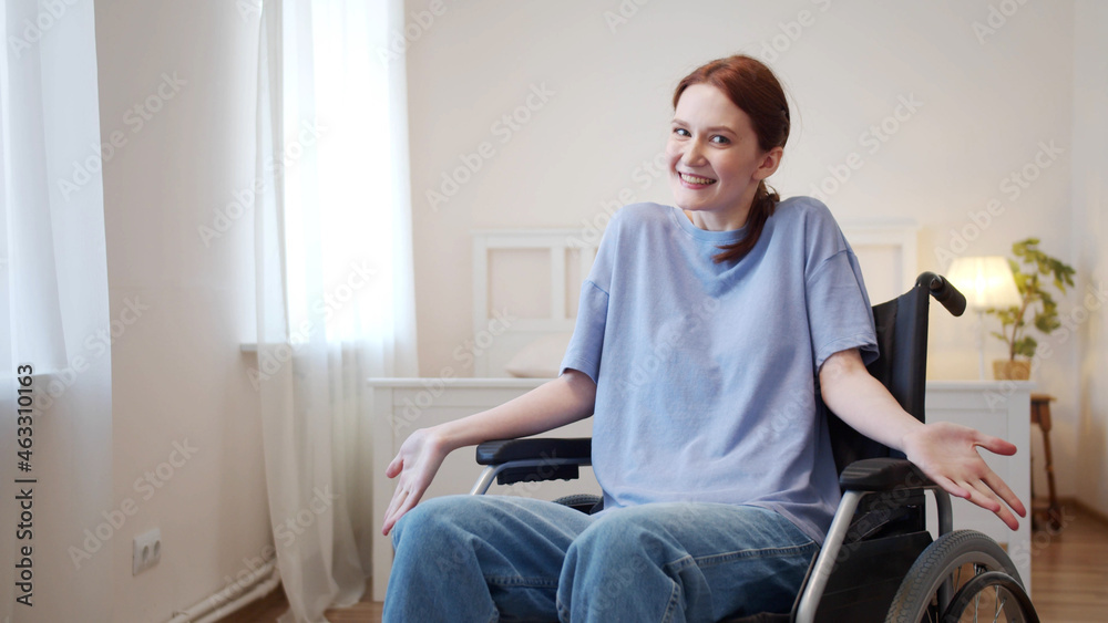 A young woman is sitting in a wheelchair and looking to the camera 