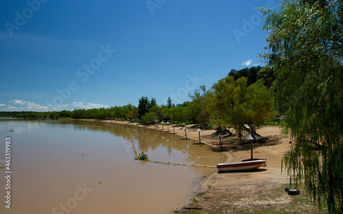 View of the river shore in a summer sunny day. A boat in the sand and the tropical jungle in the background reflected in the water. © Gonzalo