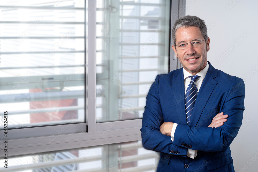 CAUCASIAN BUSINESSMAN STANDING AT THE OFFICE WITH FOLDED ARMS AND SMILING. CONCEPT OF EXECUTIVE, MANAGER, DIRECTOR OR ENTREPENEUR. CAUCASIAN BUSINESSMAN STANDING AT THE OFFICE WITH FOLDED ARMS AND SMILING. CONCEPT OF EXECUTIVE, MANAGER, DIRECTOR OR ENTREPENEUR.