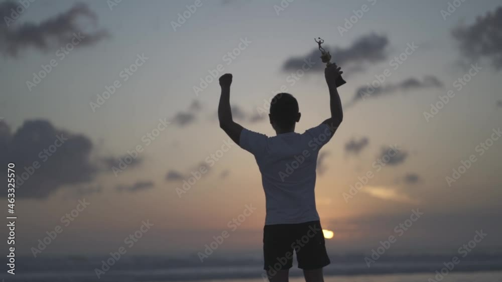 Silhouette of a proud man lifting a trophy on the beach at sunset - Winner Achievement in Slow Motion Silhouette of a proud man lifting a trophy on the beach at sunset - Winner Achievement in Slow Motion