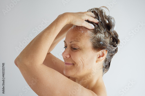 Profile view of a senior woman with bare shoulders washing her hair with shampoo