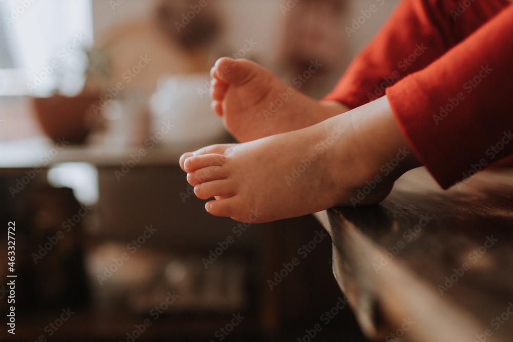 Obraz premium bare feet of a child in red trousers sitting on a wooden chair. space for text. High quality photo