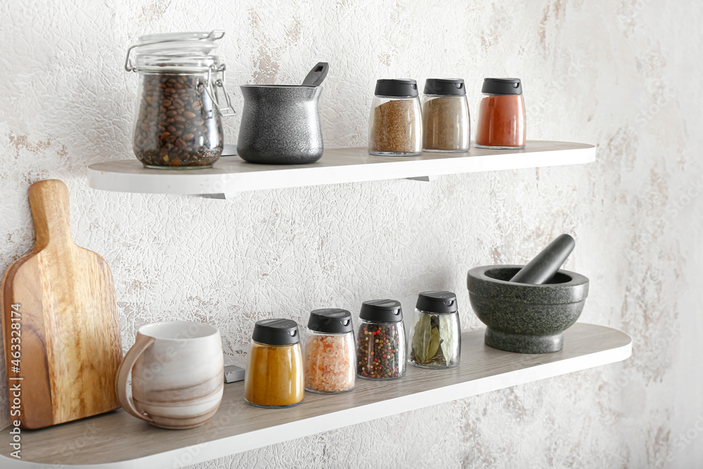 Jars with different spices, coffee beans and kitchen utensils on shelves - obrazy, fototapety, plakaty 