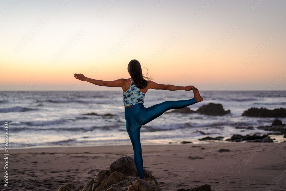 unknown latin woman stretching or doing yoga on the beach at sunset