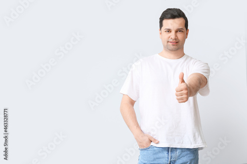 Handsome man in stylish t-shirt showing thumb-up on light background