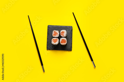 Board with delicious salmon maki rolls and chopsticks on color background