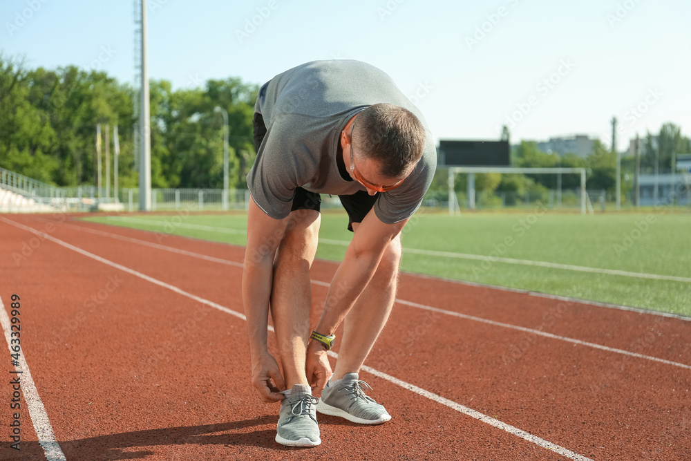 Sporty mature man adjusting sock at stadium