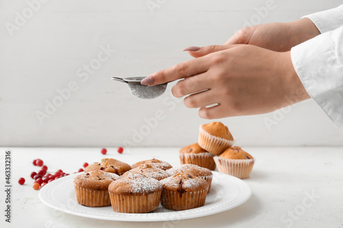 Obraz na plátne Woman sprinkling sugar powder onto delicious cranberry muffins on table