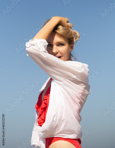 beautiful young blondie woman near the ocean in red swimsuit and white blouse