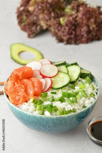 Tasty poke bowl with salmon and vegetables on light background