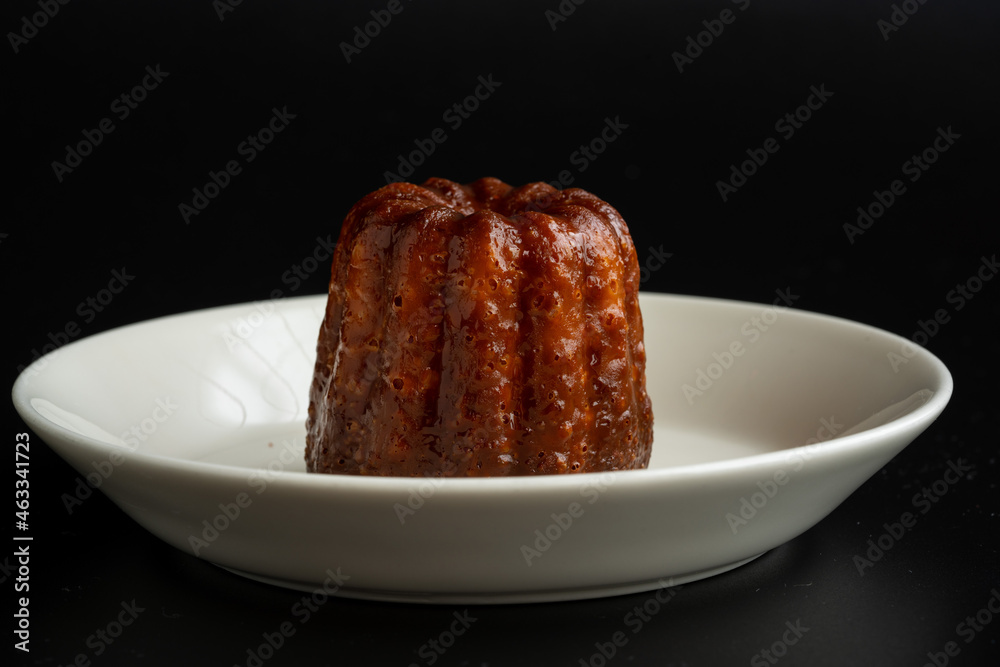 A piece of canelé on the dish with black background A piece of canelé on the dish with black background