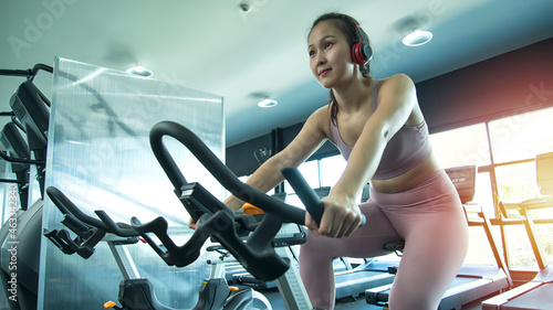 Young beautiful women with perfect bodies in sportswear looking ahead while cycling at gym.