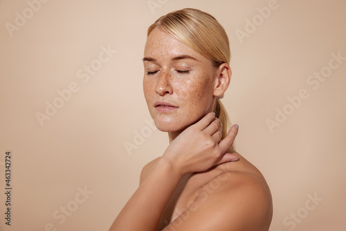 Caucasian female with freckles and blond hair standing with closed eyes massaging her neck