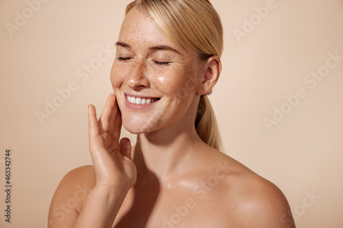 Cheerful female with blond hair massaging her cheek in studio against pastel background photo