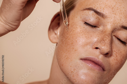 Young beautiful woman with closed eyes applying face serum with pipette photo