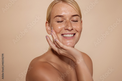 Happy woman with natural beauty skin. Smiling female touching face against pastel background in studio.