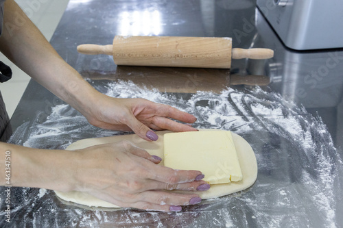 The process of rolling out puff pastry with butter layers on a table with flour and rolling pin. Workpiece for pastry and croissants